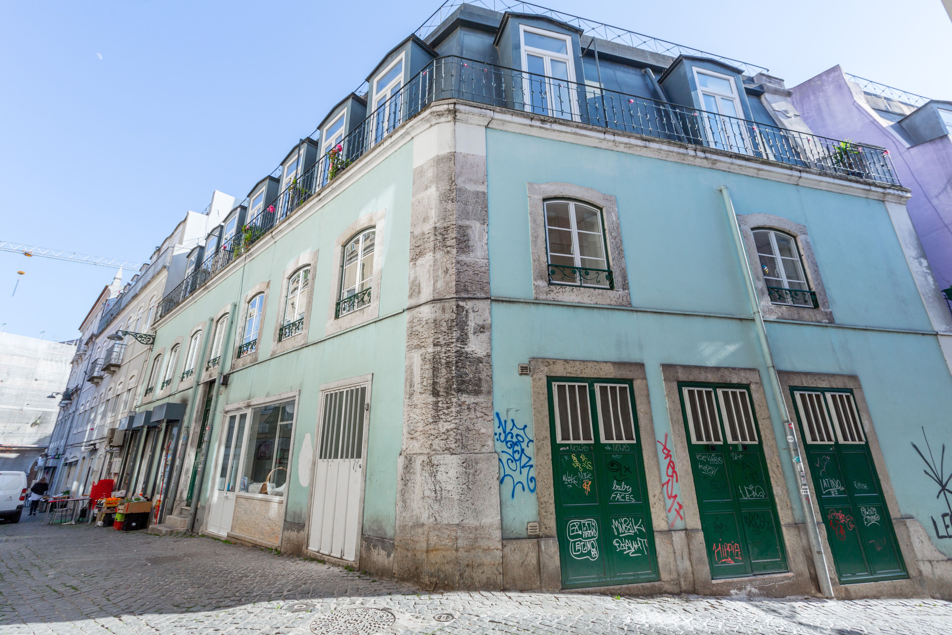 A multi-story building with a green door and windows, a balcony with railings, and a cobblestone street.