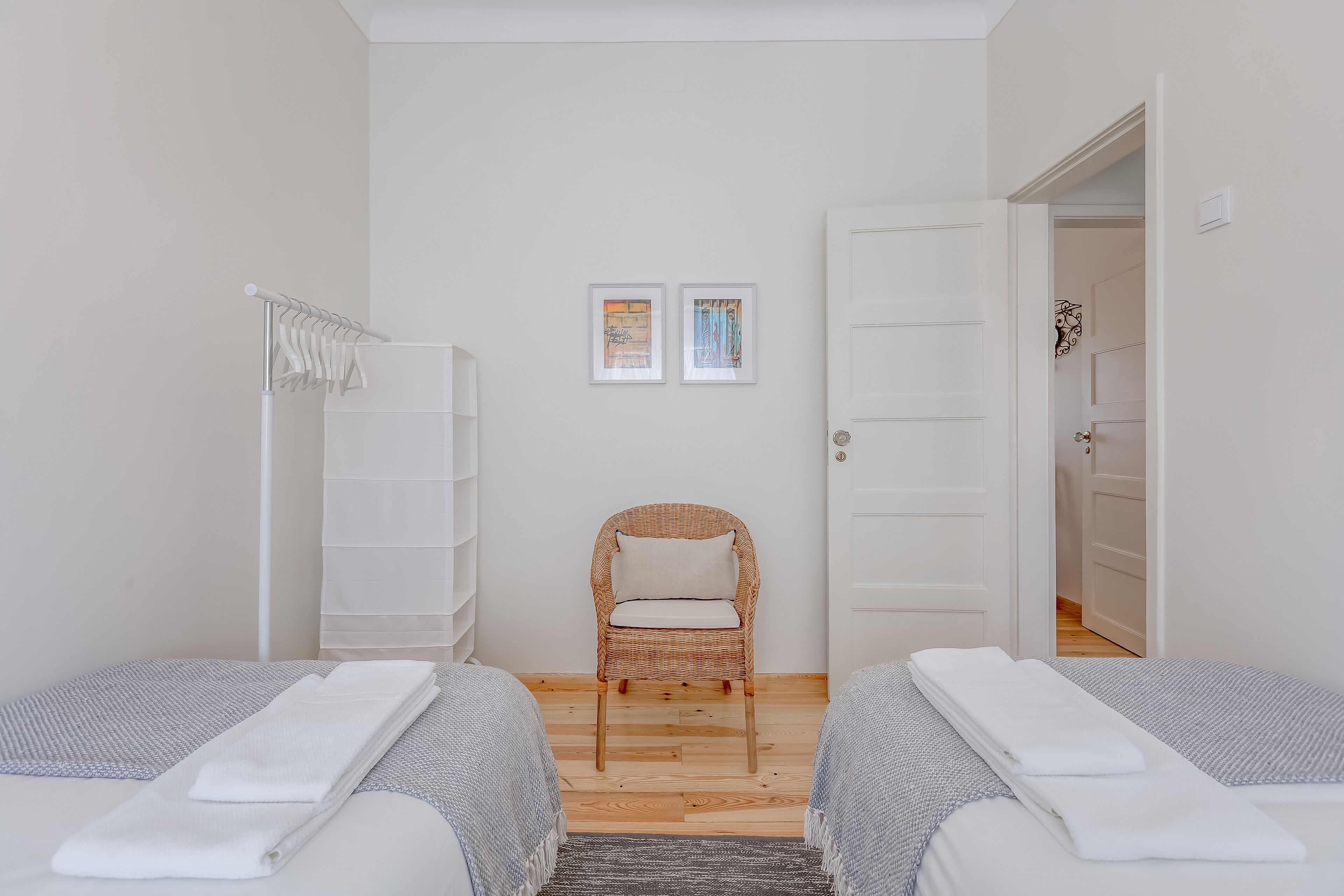 A bedroom with two beds, a chair, a wardrobe, and two framed pictures on the wall.