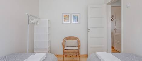 A bedroom with two beds, a chair, a wardrobe, and two framed pictures on the wall.