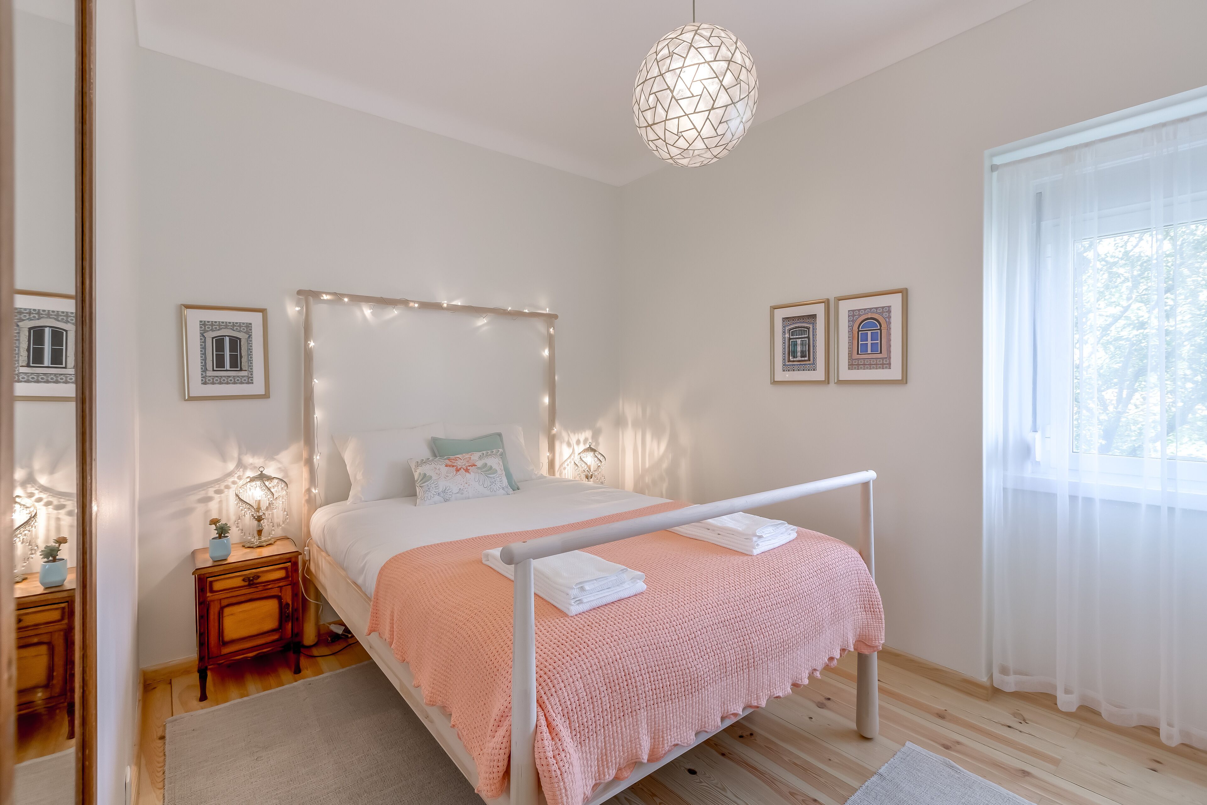 Une chambre à coucher avec un lit, des tables de chevet, un luminaire suspendu et des tableaux encadrés accrochés au mur.