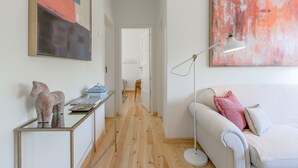 Ett modernt vardagsrum med en vit soffa, ett soffbord i glas med dekorativa föremål, en golvlampa och abstrakta tavlor på väggarna.