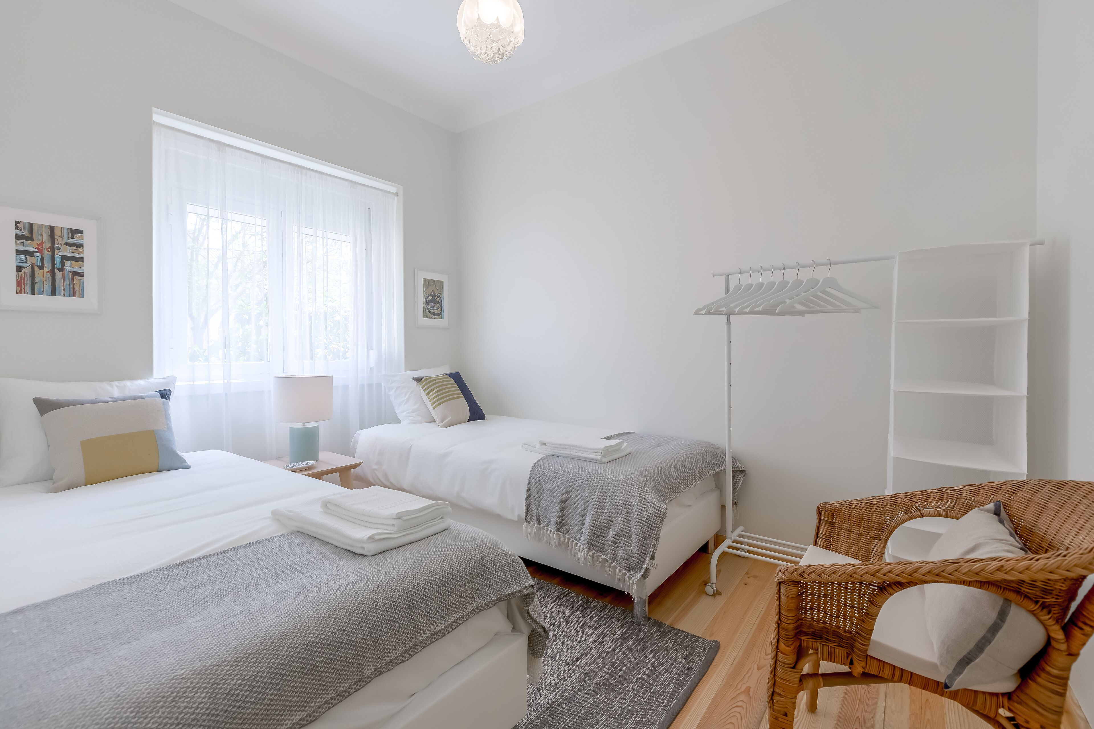 Une chambre d’hôtel avec deux lits, une chaise en osier, un lampadaire et une armoire.