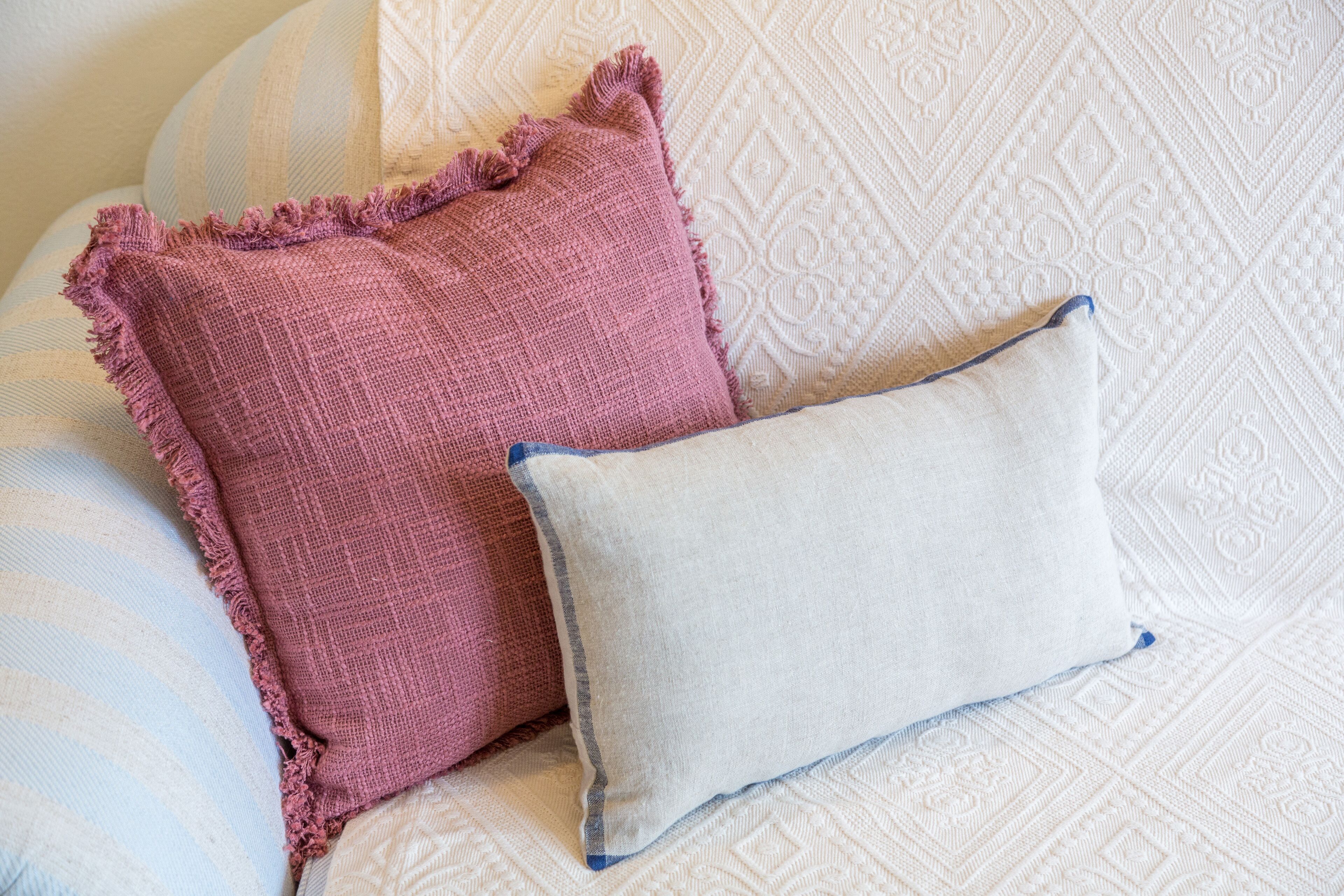A bed with a patterned bedspread and two pillows, one pink and one white.
