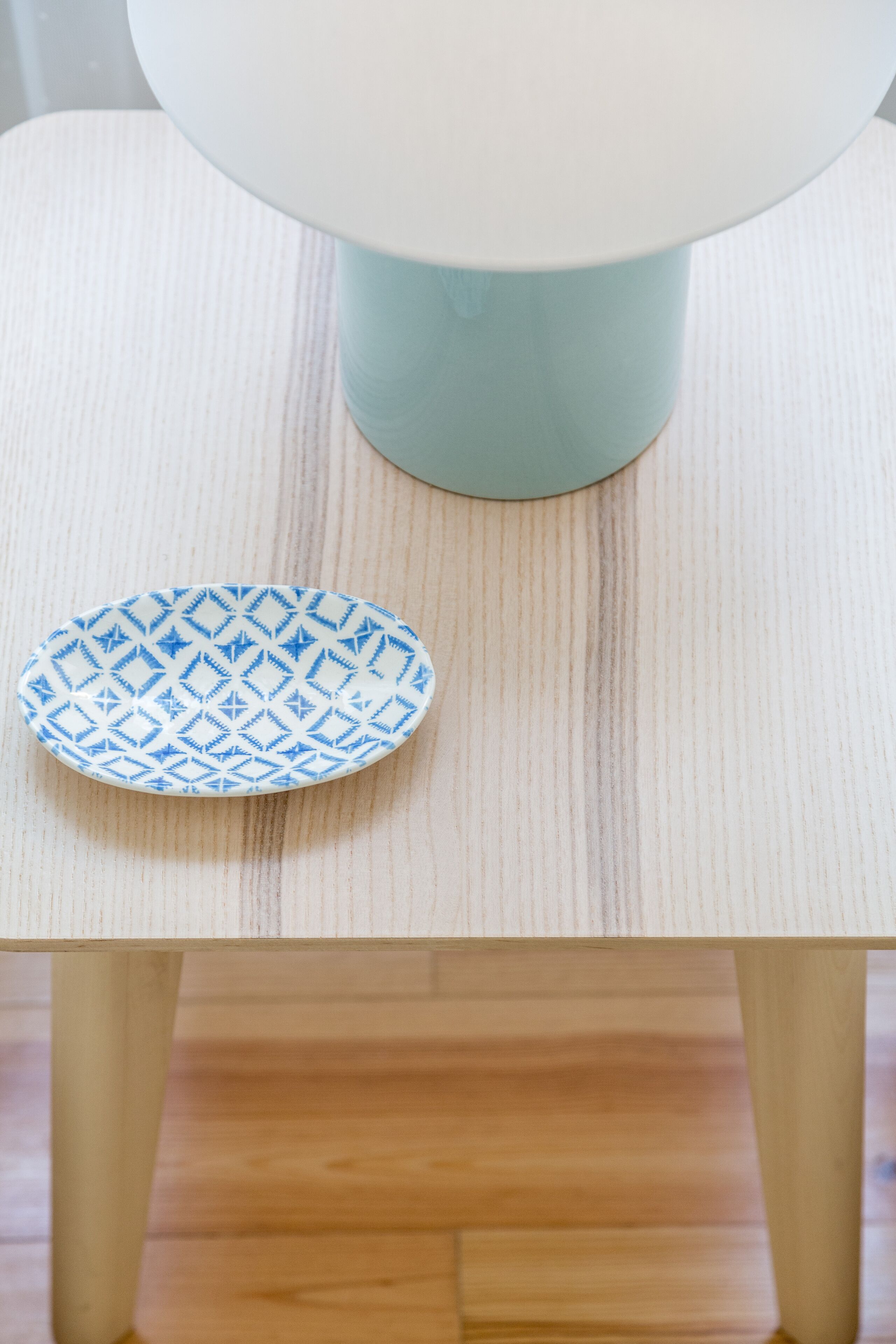 Una mesa blanca con un plato de diseño azul y una lámpara de mesa azul claro.