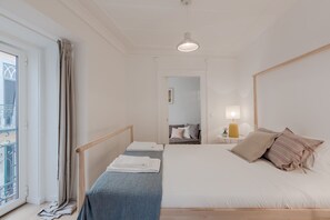 A bedroom with a bed, a bedside table with a lamp, a window with curtains, and a view of the outside balcony.