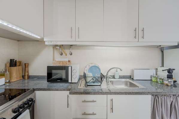 A modern kitchen with white cabinets, a granite countertop, a microwave, a toaster, and a sink. - Sunny Bairro Alto / Chiado Apartment, By TimeCooler (Lisbon)