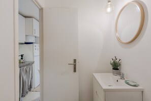 A white bathroom with a sink, mirror, and potted plant.