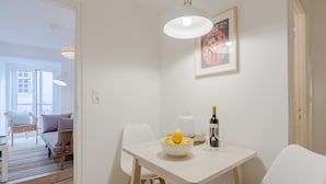 A dining area with a white table, chairs, a bowl of fruit, a bottle of wine, and a framed picture on the wall. - Sunny Bairro Alto / Chiado Apartment, By TimeCooler (Lisbon)