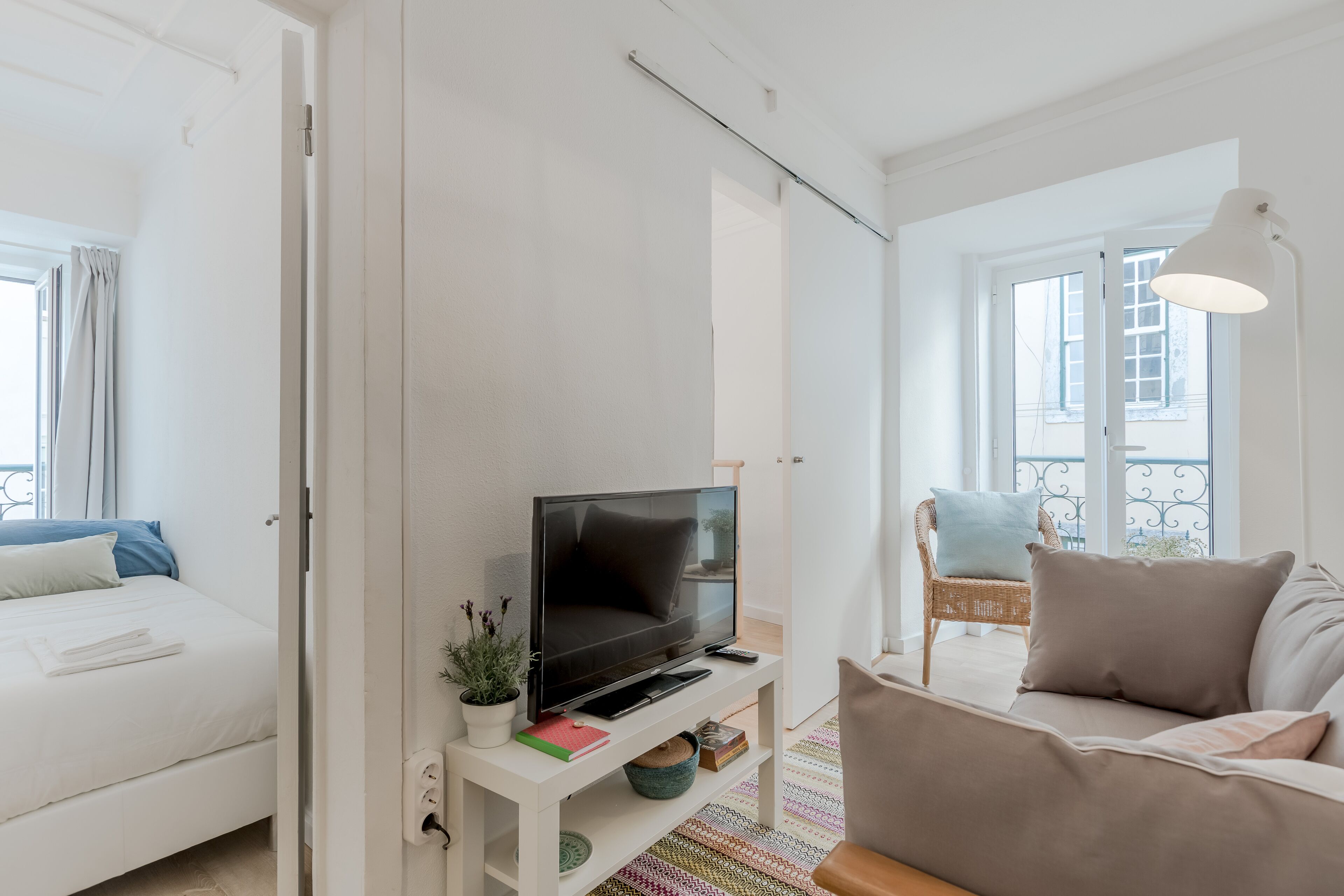 Un salon moderne avec un téléviseur à écran plat posé sur un meuble blanc, un canapé, un fauteuil et une fenêtre donnant sur la ville.