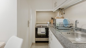A compact kitchen with a built-in oven, a sink, and a countertop with a dish rack. - Sunny Bairro Alto / Chiado Apartment, By TimeCooler (Lisbon)