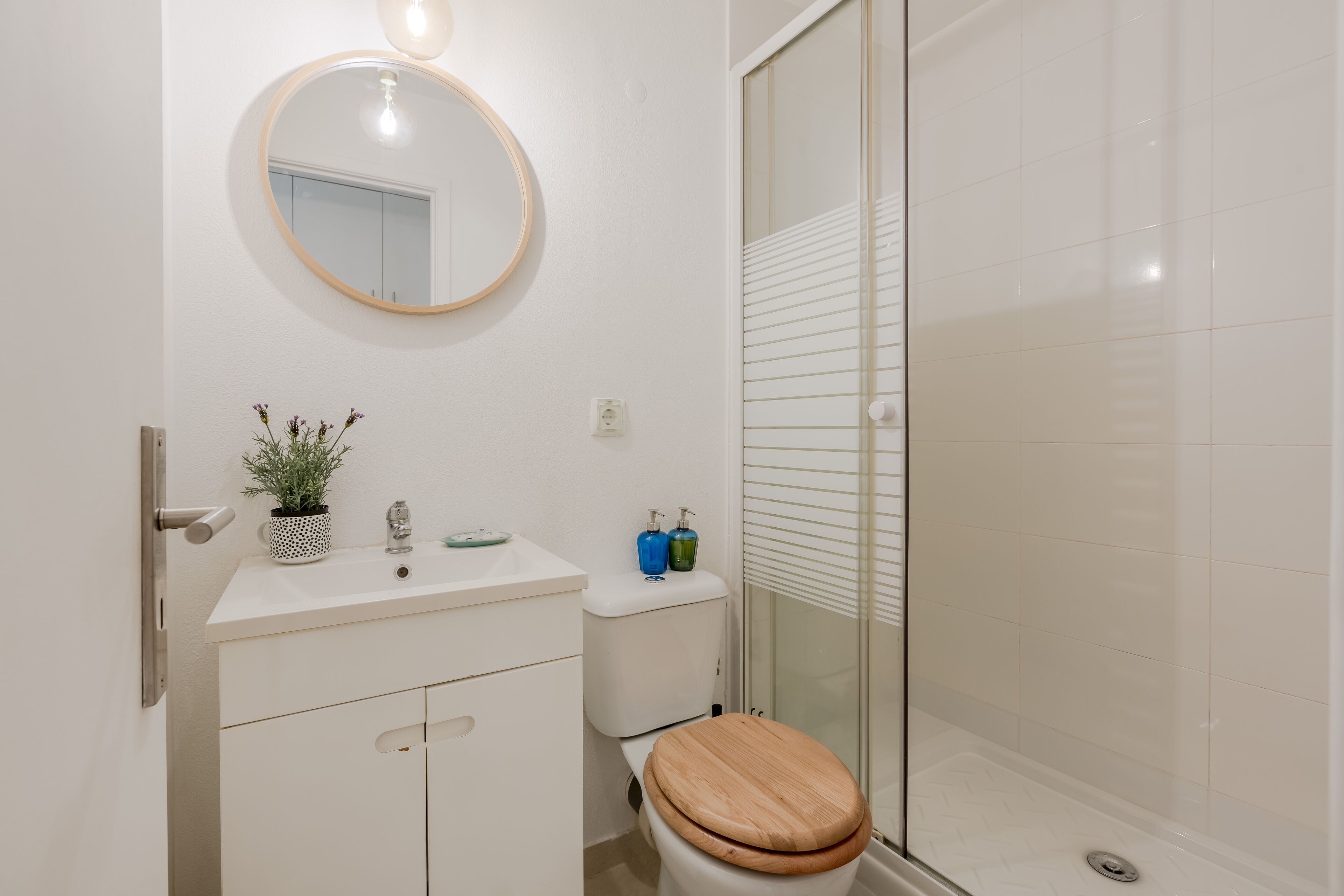 A bathroom with a toilet, sink, mirror, and shower.
