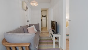 A modern living room with a grey sofa, a wooden chair, a TV on a white stand, and a patterned rug. - Sunny Bairro Alto / Chiado Apartment, By TimeCooler (Lisbon)