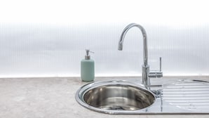 Una cocina moderna con un lavamanos de acero inoxidable, un dispensador de jabón verde y vigas de madera en el techo.