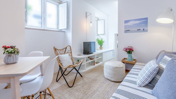 Una sala de estar moderna con un sofá blanco, una mesa de comedor, una silla de mimbre, un televisor y una estantería.