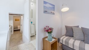 Una sala de estar moderna con un sofá, una mesita con un florero, un cuadro en la pared y un pasillo que lleva a otra habitación.