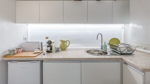 Una cocina moderna con gabinetes blancos, lavavajillas integrado, un lavamanos y una encimera con diversos utensilios de cocina.