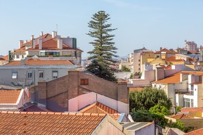 A residential area with terracotta-tiled roofs, a prominent pine tree, and a mix of building styles. - Renovated Sunny Apartment with Balcony, By TimeCooler (Lisbon)