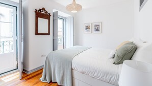 A bedroom with a bed, a hanging light fixture, a door, and a window.