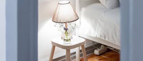 A room with a bunk bed, a small bedside table with a lamp, and a wooden floor.