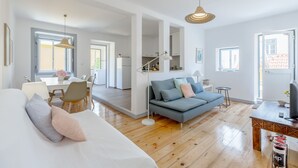 A modern living room with a sofa, dining area, and kitchen in the background. - Alfama, Bright Spacious W/ Terrace Apartment, By TimeCooler (Lisbon)