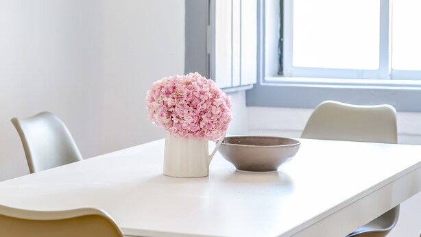 A dining table with a white vase of pink flowers and a bowl, a woven pendant light, and chairs with a mix of colors. - Alfama, Bright Spacious W/ Terrace Apartment, By TimeCooler (Lisbon)
