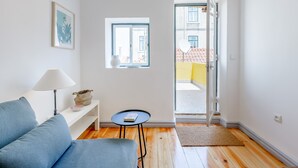 A modern living room with a blue sofa, a small round table with a book, a white lamp, and a framed picture on the wall. - Alfama, Bright Spacious W/ Terrace Apartment, By TimeCooler (Lisbon)