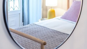 A circular mirror reflecting a bed with a wooden headboard, a yellow bedside lamp, and a window with blue curtains. - Alfama, Bright Spacious W/ Terrace Apartment, By TimeCooler (Lisbon)