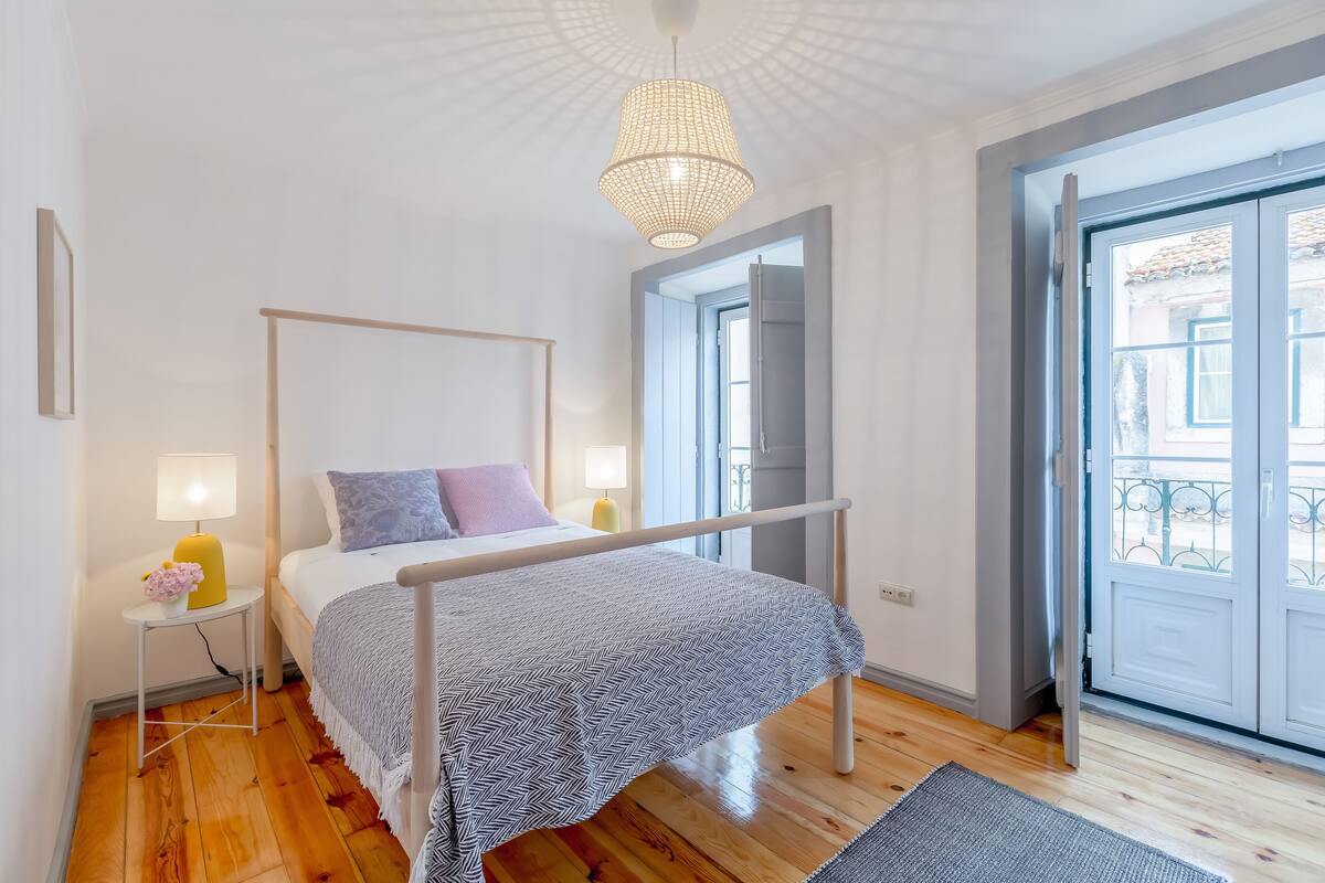 A modern bedroom with a metal bed frame, a bedside table with a lamp, and a view of the outside through a large door.