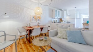 Una sala de estar moderna con un sofá blanco, una mesa de comedor con sillas y una cocina al fondo.