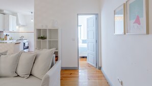 Una sala de estar moderna y minimalista con un sofá, una zona de cocina y un pasillo que conduce a un dormitorio.