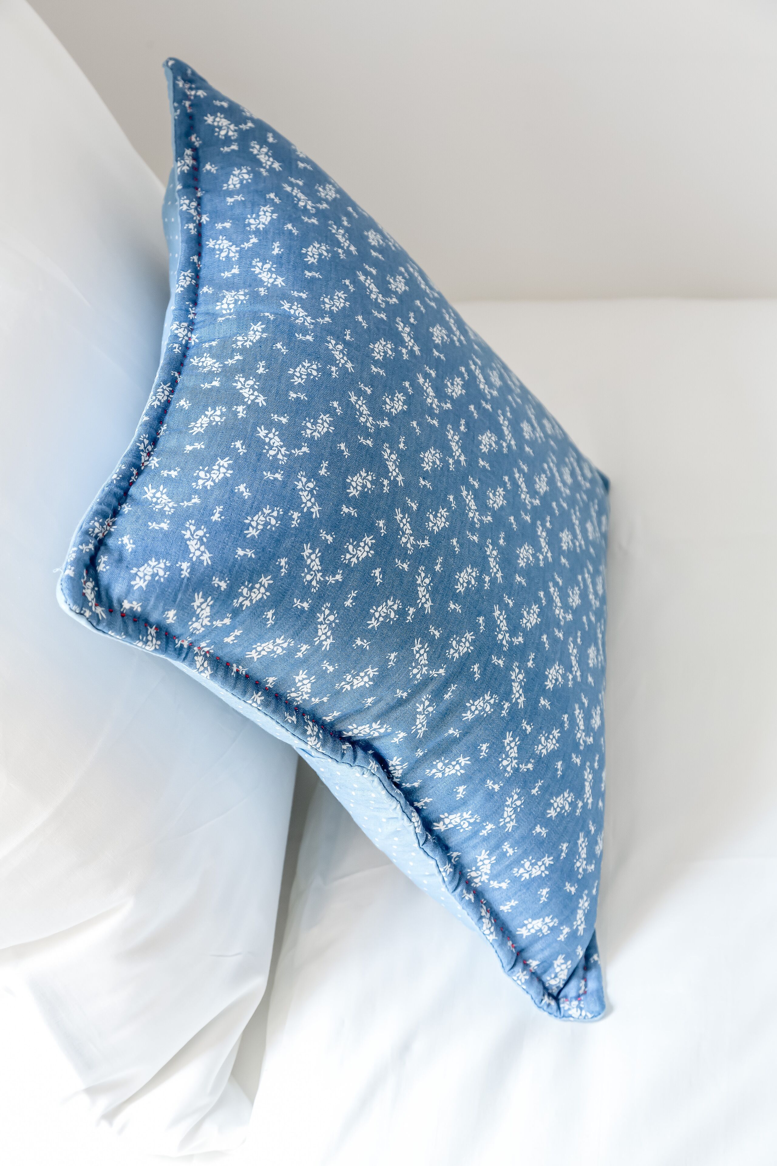 Un almohadón con estampado floral sobre una cama con sábanas blancas.