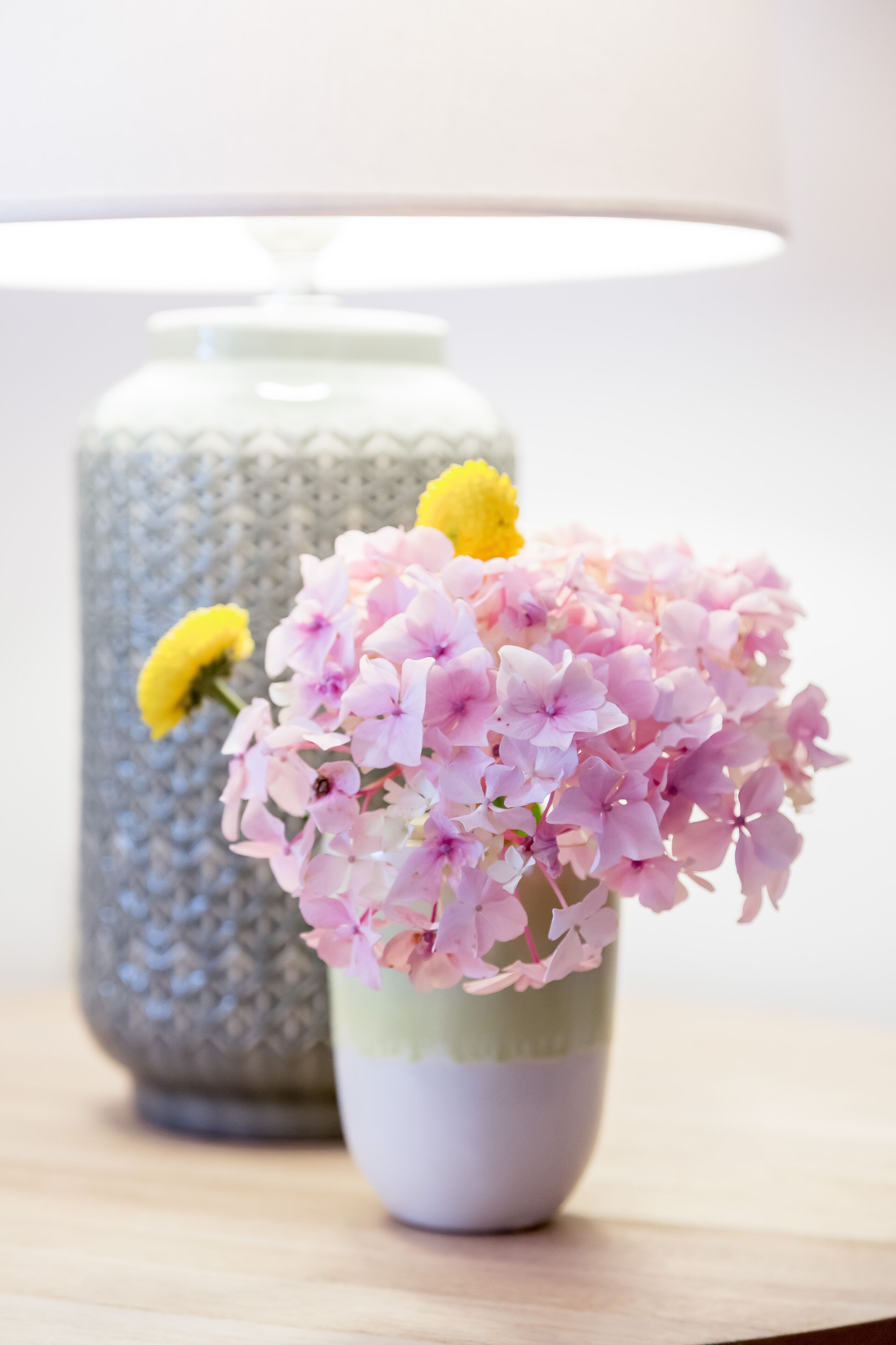 A vase with pink flowers and a yellow flower on a table.