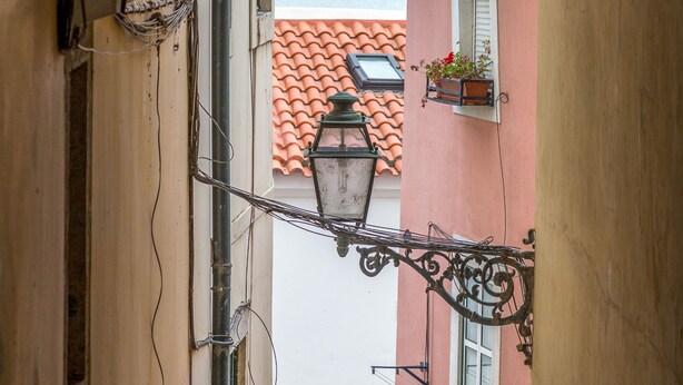Un estrecho callejón con vista al mar a través de un arco, un techo de tejas y un farol colgante.