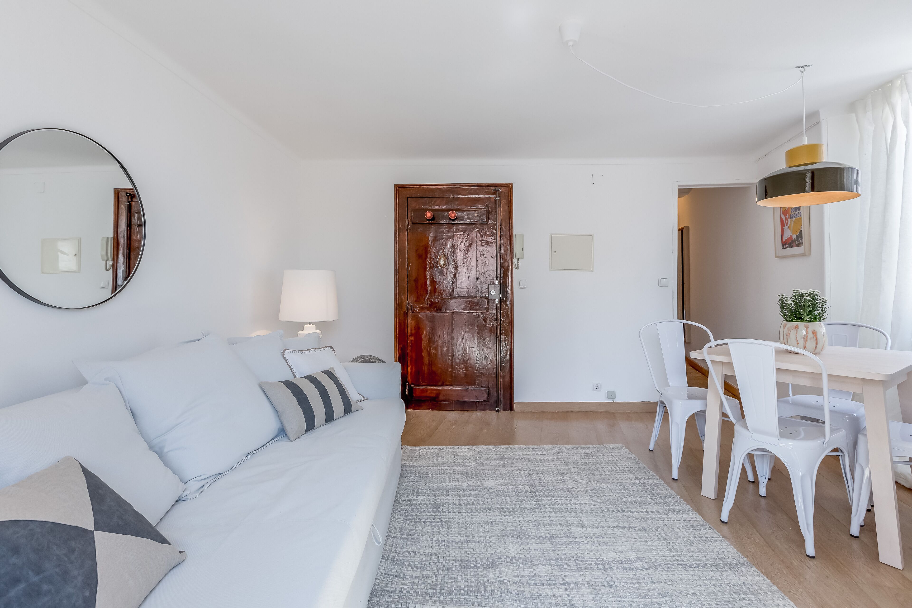 Een moderne woonkamer met een bank, een eettafel met stoelen, een houten deur en een spiegel aan de muur.