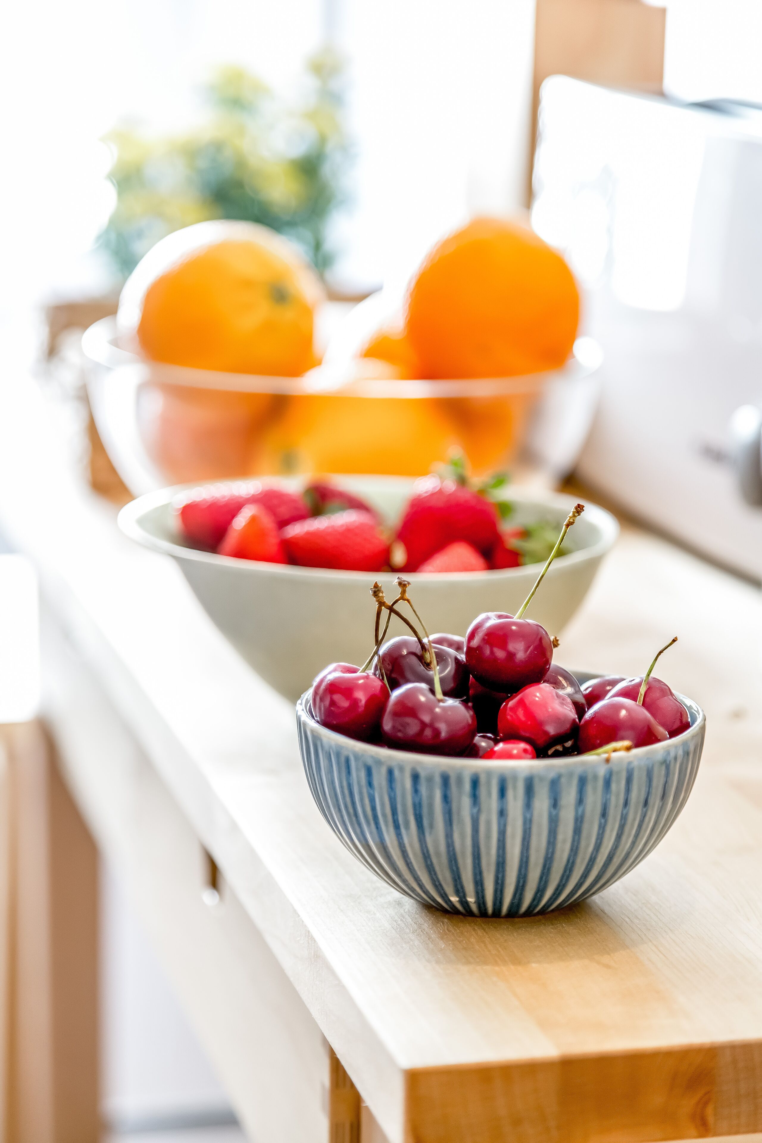 A kitchen counter with a bowl of cherries and a bowl of strawberries and oranges.