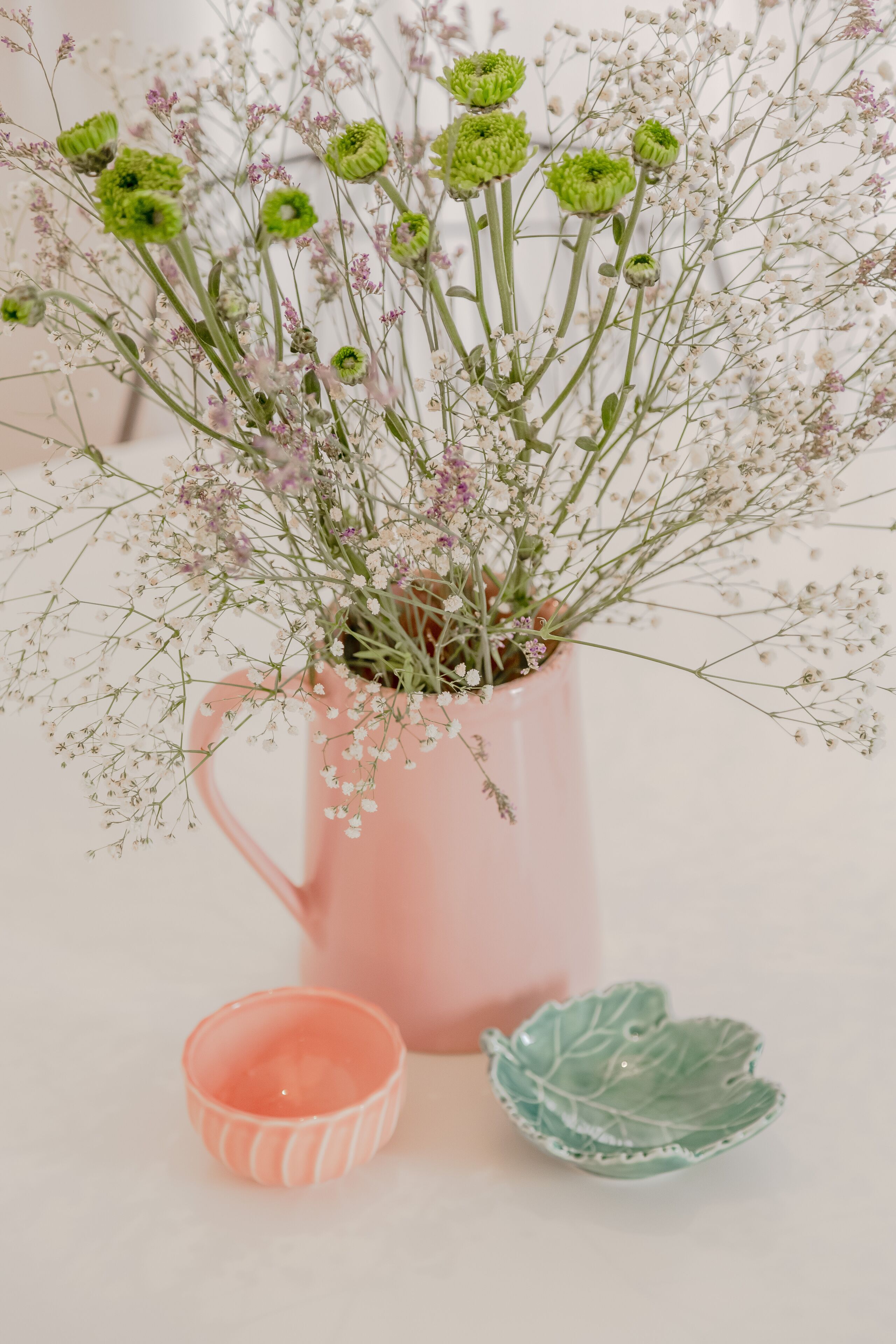 A pink vase with green and white flowers, a small pink candle holder, and a green leaf-shaped dish.