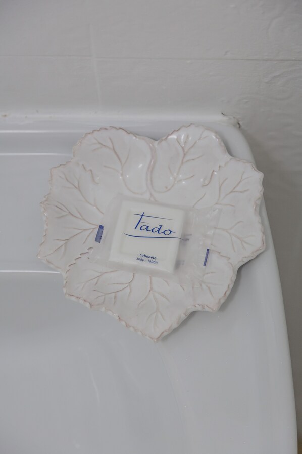 Een witte keramieken zeepbakje met een bladpatroon en een etiket met de tekst 'tado soap - soap - jabón'.