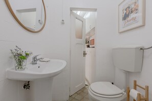 A bathroom with a white sink, mirror, and toilet. There is a framed picture on the wall and a small plant on the sink. - Typical Alfama Apartment, By TimeCooler (Lisbon)