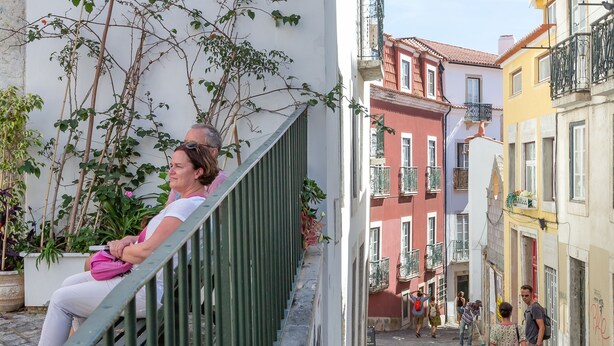 A narrow cobblestone street with buildings on either side, a metal railing, and a street lamp. - Typical Alfama Apartment, By TimeCooler (Lisbon)