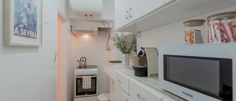 Een moderne keuken met witte kasten, een magnetron en een fornuis. Aan de muur hangt een lijst en op het aanrecht staat een kleine plant.