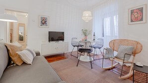 A modern living room with a sofa, dining table, chairs, and a TV. - Typical Alfama Apartment, By TimeCooler (Lisbon)