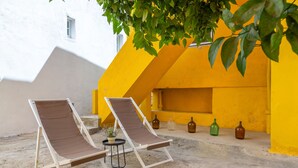 Two lounge chairs under a tree, a small table with a plant, and three bottles on a ledge. - Bright & Spacious W/ Orange Tree Patio Apartment by TimeCooler (Lisbon)