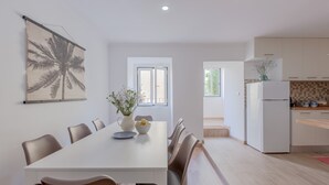 A modern kitchen with white cabinets, a white refrigerator, and a dining area with a white table and chairs. - Bright & Spacious W/ Orange Tree Patio Apartment by TimeCooler (Lisbon)