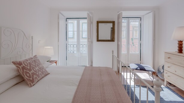 A bedroom with a bed, bedside table, dresser, and a window with a view. - Bright & Spacious W/ Orange Tree Patio Apartment by TimeCooler (Lisbon)