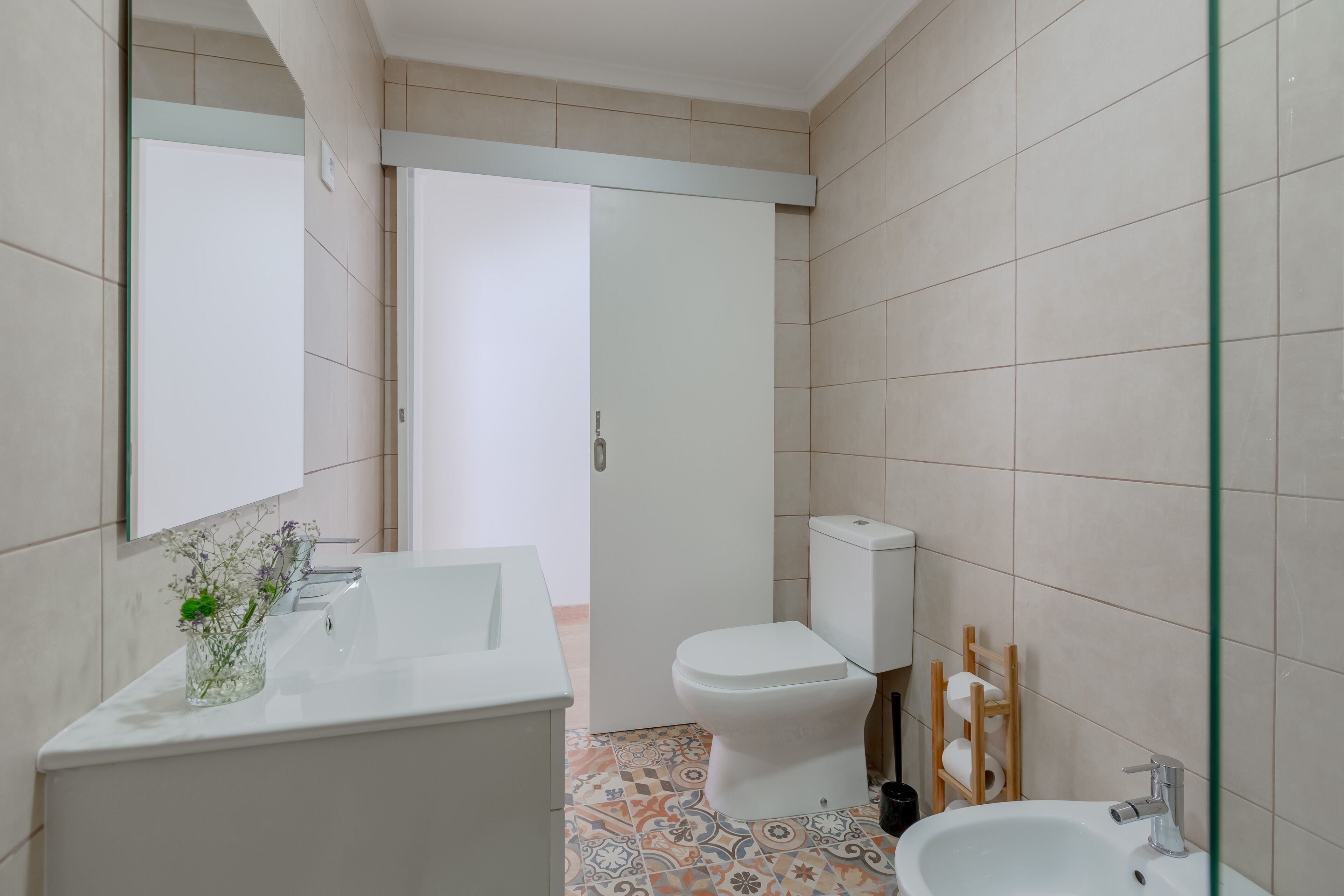Ein modernes Badezimmer mit Waschbecken, Toilette und Badewanne in Weiß. Der Boden weist ein geometrisches Fliesenmuster auf.