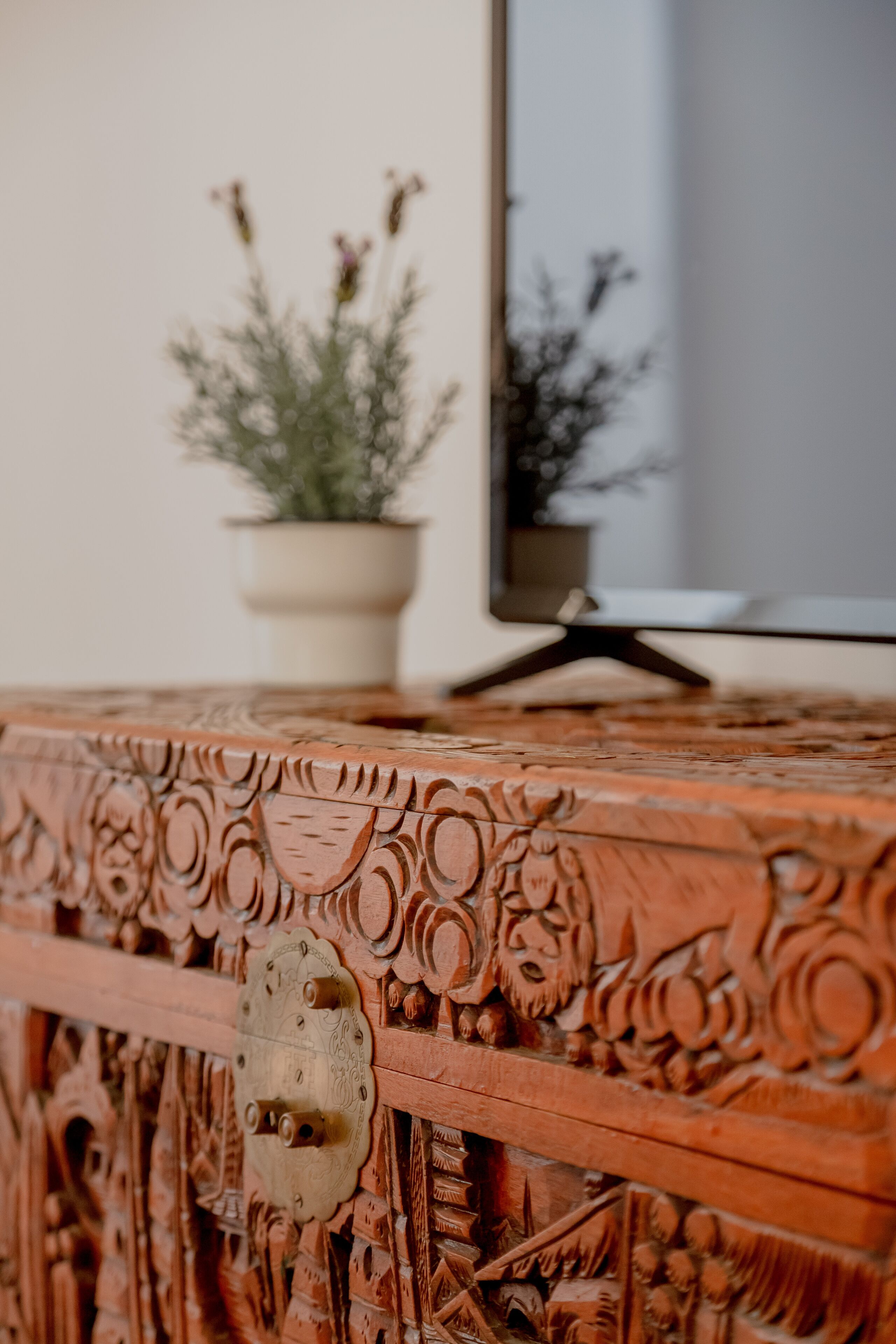 Una mesa de madera con intrincados grabados y una planta en maceta al fondo.