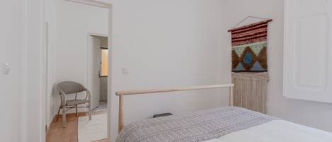 A bedroom with a bed, a chair, a hanging tapestry, and a door leading to another room.