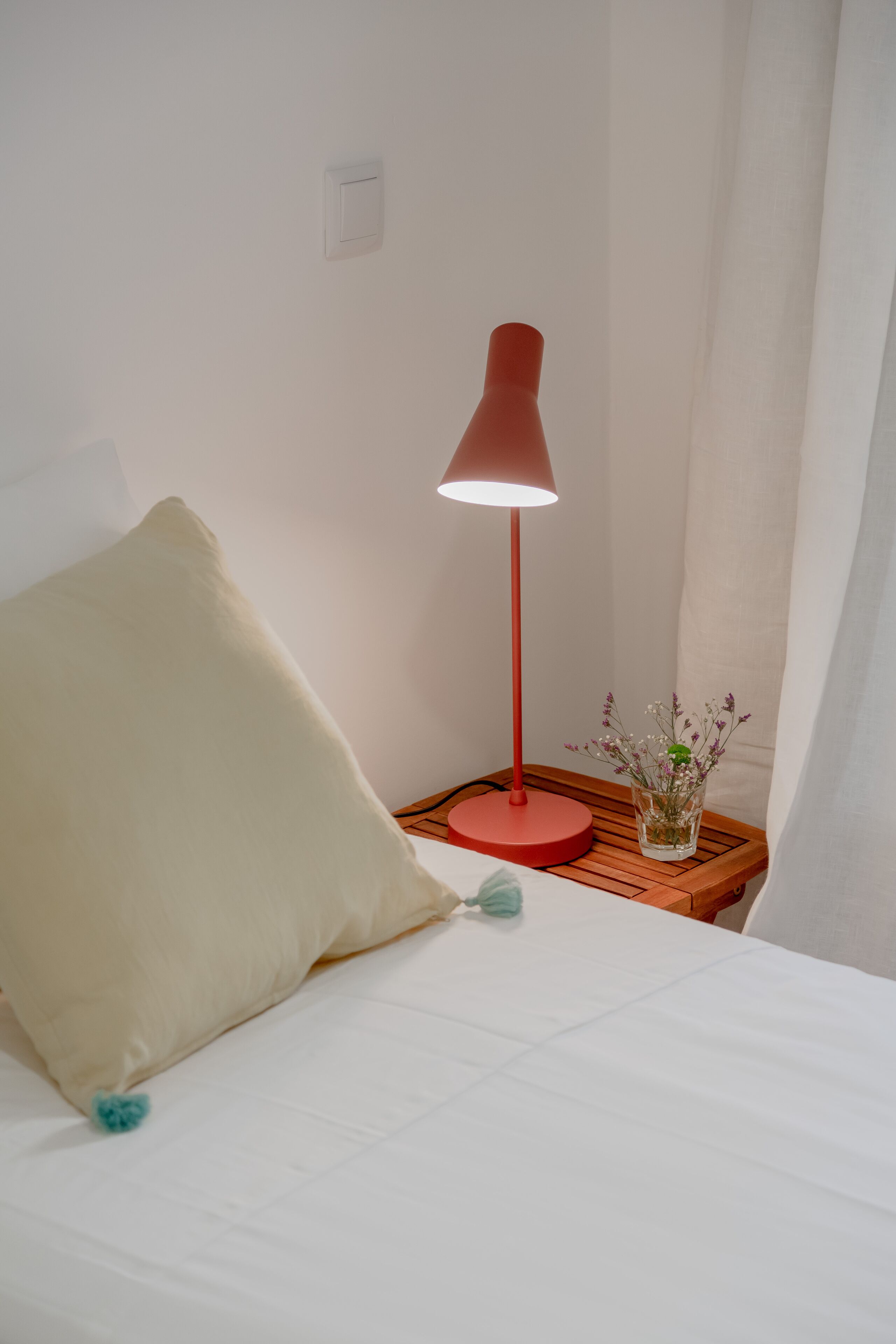 A bed with a white pillow and a red lamp beside it.