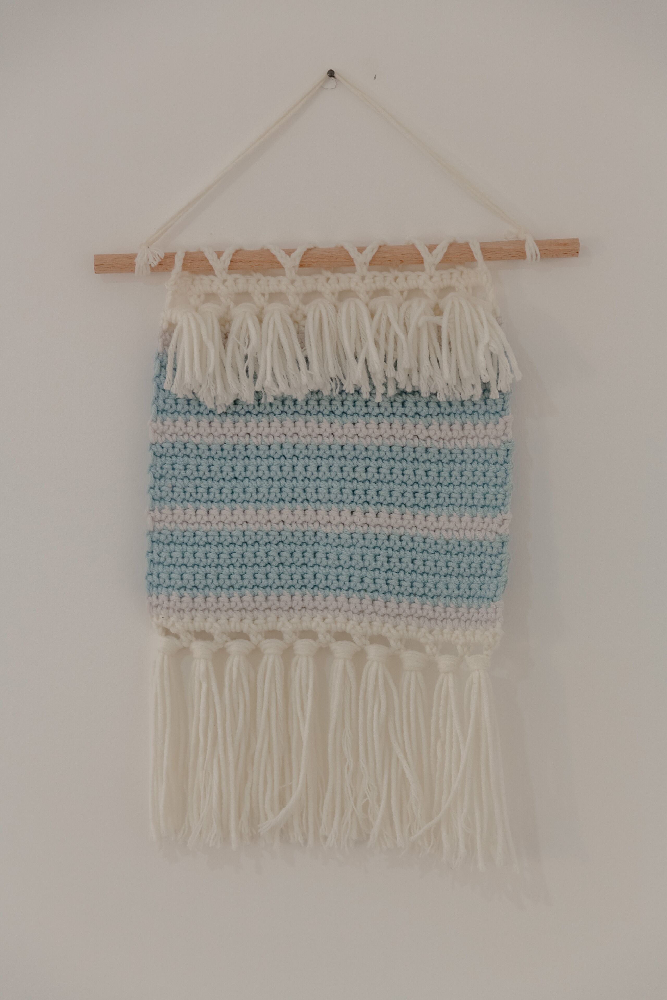 Un colgador de macramé con una vara de madera y borlas blancas.