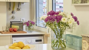 A modern kitchen with a large window, a bowl of fruit, a vase of flowers, and a coffee machine. - Light Apartment W/ Balcony Apartment by TimeCooler (Lisbon)
